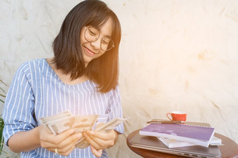 Young woman smiling as she counts cash in her hands UVKu393