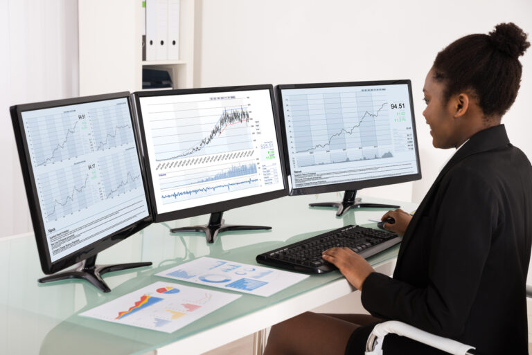 analyst analyzing stock charts on three desktop screens