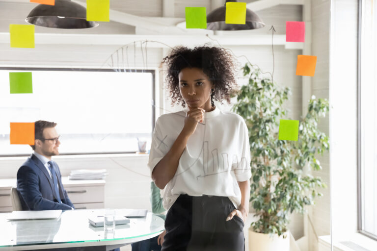 investor considers writing on glass wall while another sits in the background