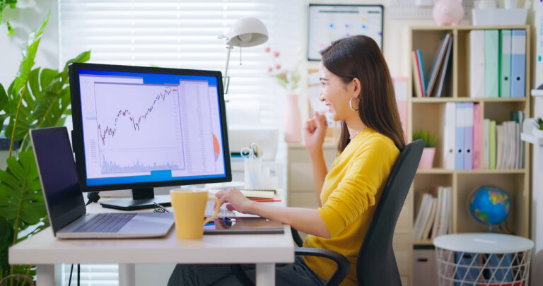 smiling person looking at a monitor with stock chart